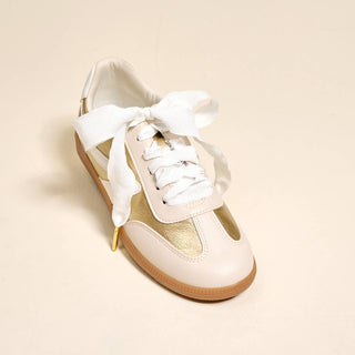 White sneaker with gold accents on a beige background