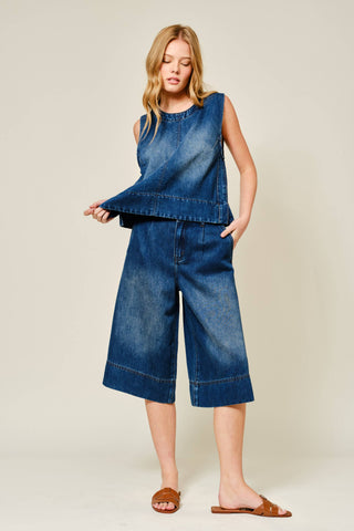 Woman wearing a blue denim sleeveless top and wide-leg jeans on a beige background