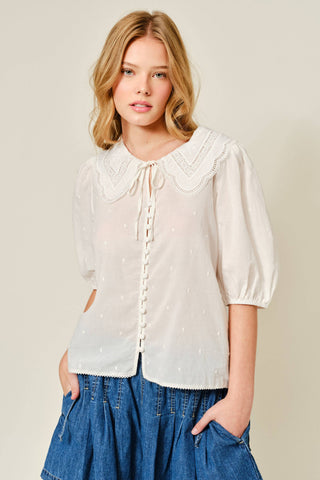 Woman wearing a white blouse with a lace collar and blue jeans on a beige background