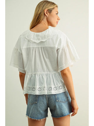Woman wearing a white embroidered blouse and denim shorts on a plain background