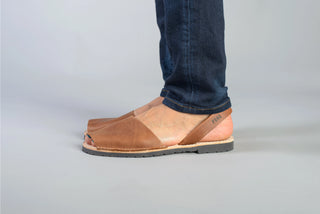Brown leather sandals worn with blue jeans on a gray background