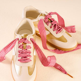 White sneakers with red and white checkered laces on a beige background