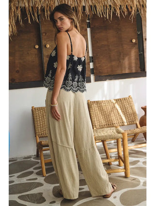 Woman in a black and white patterned top and beige pants standing in a rustic interior setting.