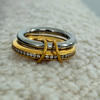 Three interlocking rings in gold, silver, and rose gold on a textured surface.