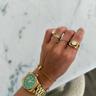Hand wearing a gold watch and multiple rings on a marble surface