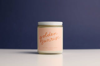 Candle jar labeled 'golden sunrise' on a reflective surface with a dark blue background