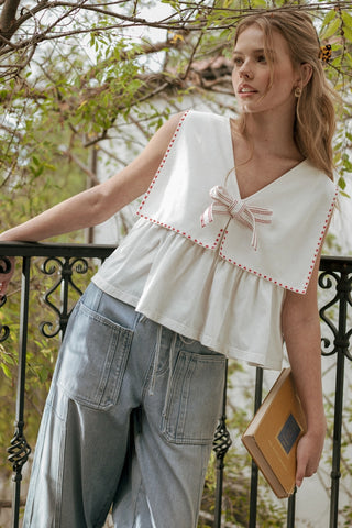 Woman wearing a white blouse with red trim and gray pants, standing outdoors.