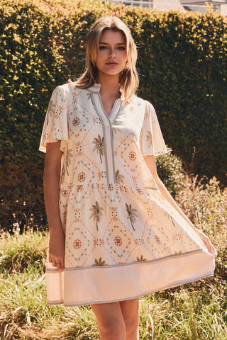 Woman wearing a patterned dress standing in a grassy area with bushes in the background