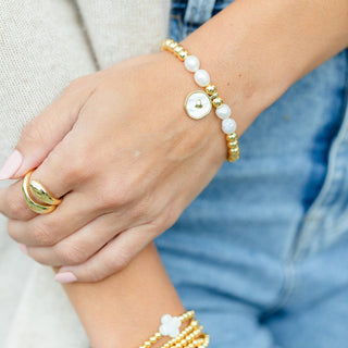 Close-up of a wrist wearing a gold and white beaded bracelet with a blurred background