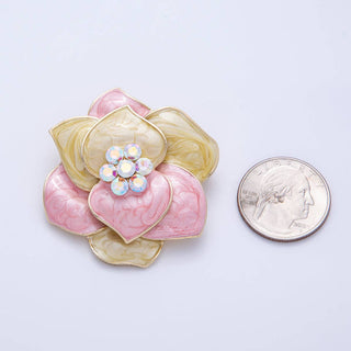 Decorative brooch with pink and gold colors next to a quarter for scale on a light gray background