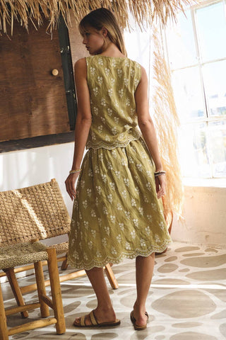 Woman in a green dress standing in a room with a thatched roof and wooden furniture.