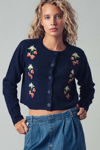 Woman wearing a navy blue cardigan with floral embroidery on a plain background