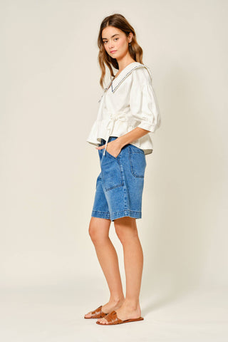 Woman wearing a white blouse and blue denim shorts on a plain background