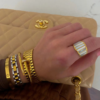 Hand with gold jewelry holding a beige quilted handbag with Chanel logo.