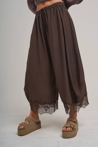 Brown wide-leg pants with lace trim worn by a person on a plain background