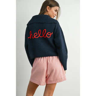 Woman wearing a navy jacket with 'hello' in red on the back, paired with pink shorts.