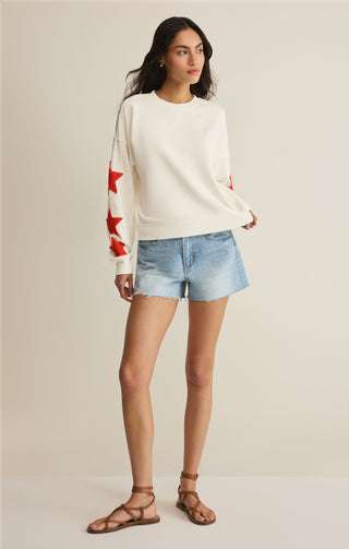 Woman wearing a white sweater with red star patterns and denim shorts on a beige background