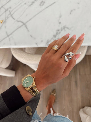 Hand wearing a gold watch and silver ring with a marble background