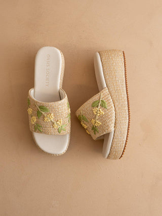 Pair of raffia sandals with floral embroidery on a beige background