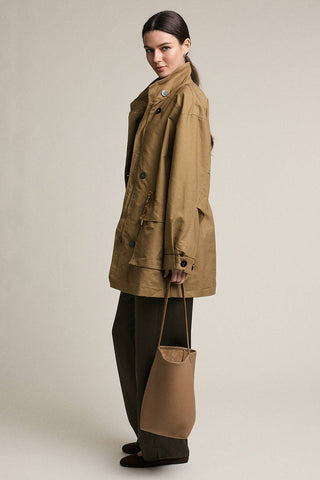 Woman wearing a brown coat holding a matching bag against a plain background