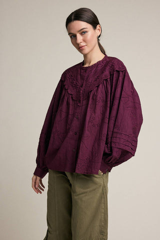 Woman wearing a burgundy blouse with lace details on a beige background