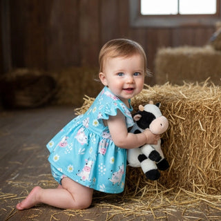 baby in barn wearing blue romper holding cow