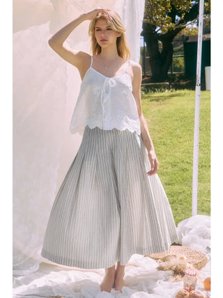 Woman wearing a white top and gray pleated skirt standing outdoors.