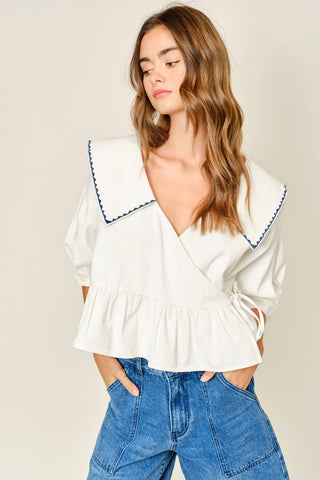 Woman wearing a white blouse with blue trim and blue jeans against a beige background