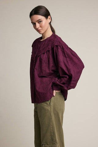 Woman wearing a burgundy blouse with puffed sleeves and green pants on a beige background