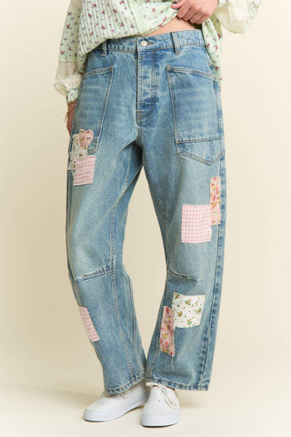 Blue jeans with patchwork design worn by a person on a plain background