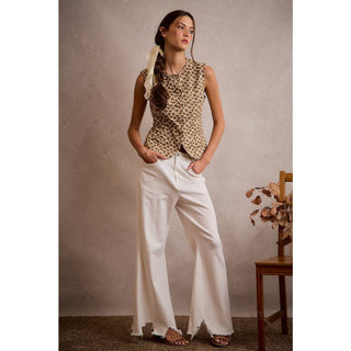Woman wearing a patterned top and white pants against a neutral background