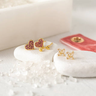 Gold heart-shaped earrings with red gemstones on a white surface