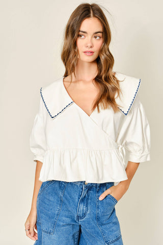 Woman wearing a white blouse with ruffled details and blue jeans on a beige background