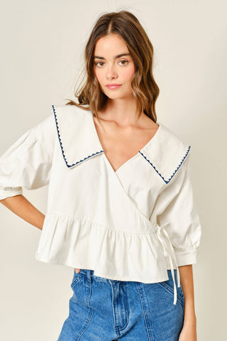 Woman wearing a white blouse with blue trim and blue jeans on a plain background