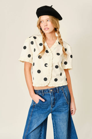 Woman wearing a polka dot blouse, black beret, and blue jeans against a plain background