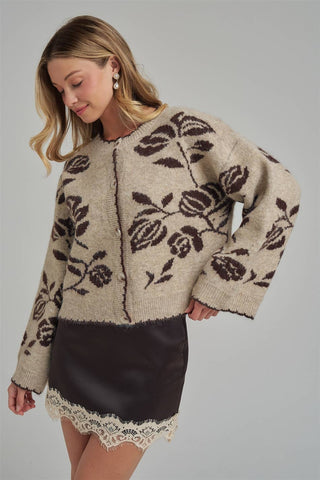 Woman wearing a beige cardigan with floral patterns on a gray background