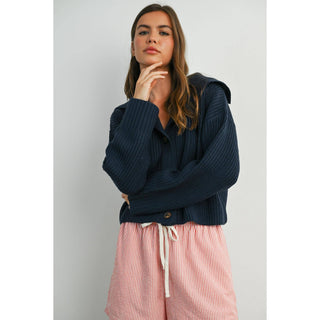 Woman wearing a navy blue ribbed sweater and pink striped pants against a light gray background