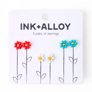 Packaged earrings with floral designs on a white background, featuring the brand 'INK+ALLOY'.