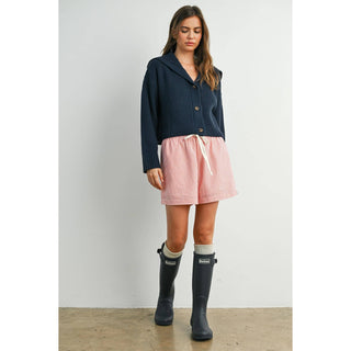 Woman wearing a navy cardigan, pink skirt, and black rain boots against a white background