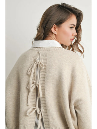 woman wearing beige sweater with ties in back on white background.