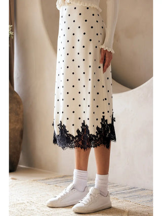 Person wearing a polka dot skirt with lace trim and white sneakers indoors.
