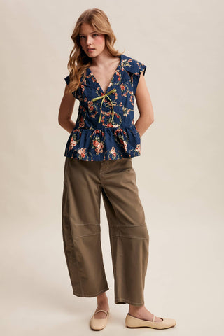 Woman wearing a floral top and brown pants on a beige background