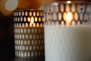 Two candles, one with a polka dot pattern and the other plain, burning against a dark background.