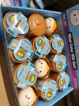 Box of colorful toy figures with labels, likely educational, on a cardboard surface.