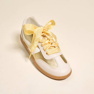 White sneaker with yellow checkered laces on a beige background