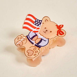 Teddy bear figurine with American flag and red bow on a beige background