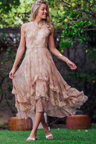 Woman in a flowing dress standing outdoors with greenery in the background