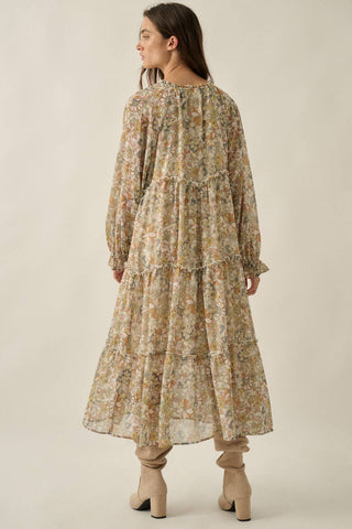 A woman shown from the back wearing a long-sleeved, tiered midi dress with a beige and brown floral pattern, paired with beige boots, against a plain beige studio background.