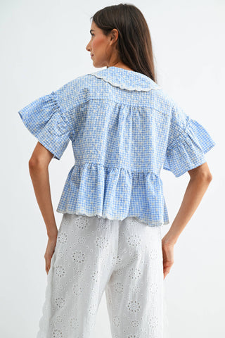 Woman wearing a blue checkered blouse with ruffled details on a white background