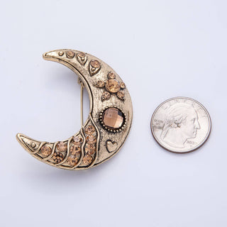 Decorative crescent moon brooch with brown gemstones next to a quarter for scale on a white background